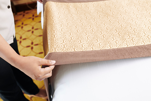 Close-up of maid making the bed in the hotel room or putting the duvet on the bed