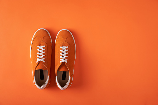 Top view of casual orange suede trainers on grey wooden planks