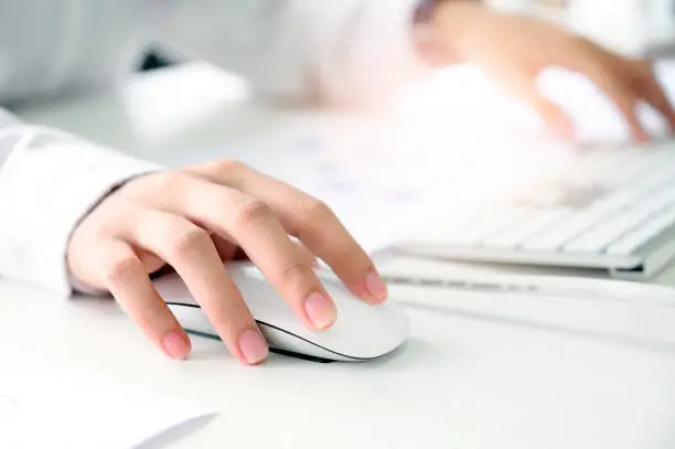 Closeup shot of female hand holding mouse and working with desktop computer while sitting at office desk.