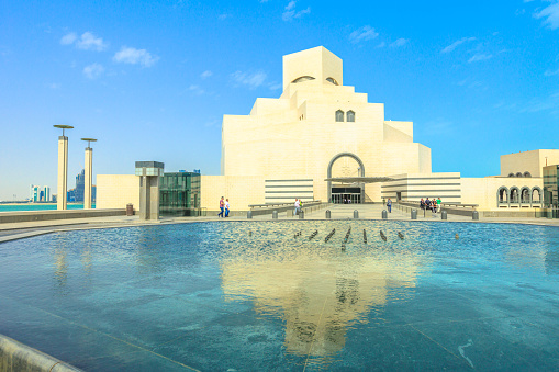 Doha, Qatar - February 16, 2019: Museum of Islamic Art, popular tourist attraction along Corniche in Doha city reflecting on fountain water in a sunny day. Middle East, Arabian Peninsula, Persian Gulf