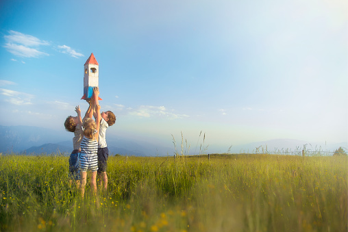 Three Children Playing with a Toy Space Rocket in the Meadow in Italian Dolomites Mountains