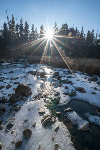 Photo of Young woman yoga posing on rock above frozen river in the forest looking at sunset