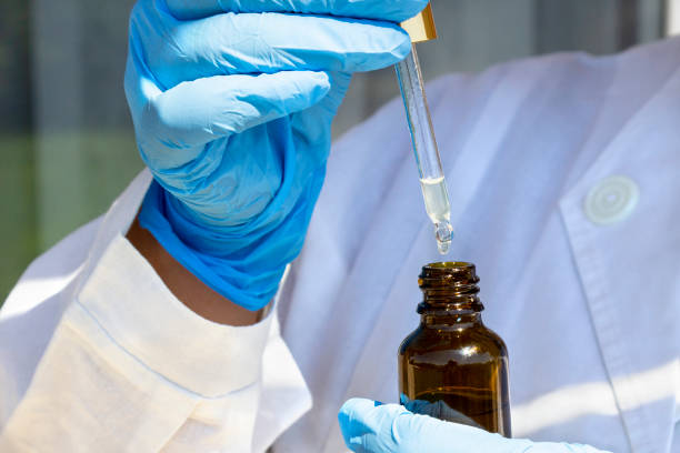 茶色のガラス瓶の上に天然油の滴とピペットドロッパーを保持する白いコートと青い医療手袋の女性の手 - 2605 ストックフォトと画像
