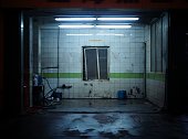 Dirty greasy garage car washing repair shop with white and green tiles and skewed window in darkness