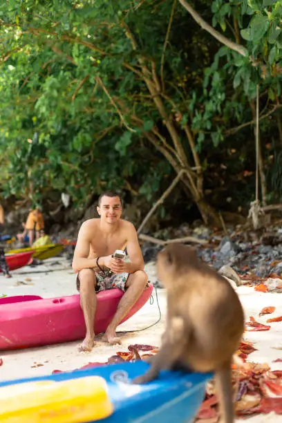 A tourist looks at Monkey sitting on the tip of a canoe waiting for food from tourists. Monkey Beach on Tropical Island.