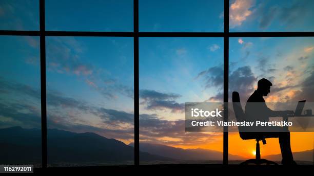 The Man Working At The Table Near A Window On A Mountain Sunset Background Stock Photo - Download Image Now