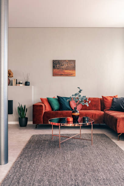 istock Stylish round table with flowers next to corner sofa with emerald pillows 1162199389