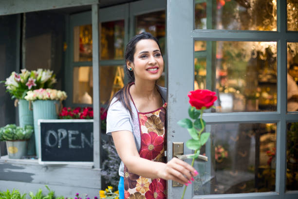 флорист женского пола с красной розой в дверях цветочного магазина - owner florist sign business стоковые фото и изображения