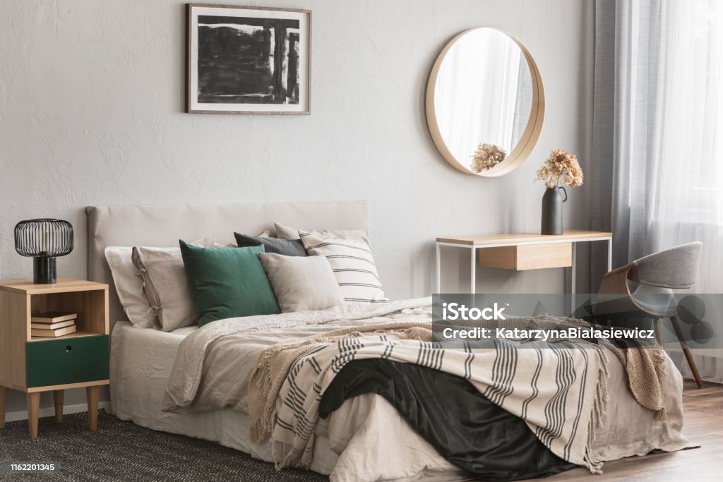 Eleganckie okrągłe lustro w drewnianej ramie nad fantazyjnym stołem konsolowym z kwiatami w wazonie w modnym wnętrzu sypialni z beżowym wazonem - Zbiór zdjęć royalty-free (Sypialnia)