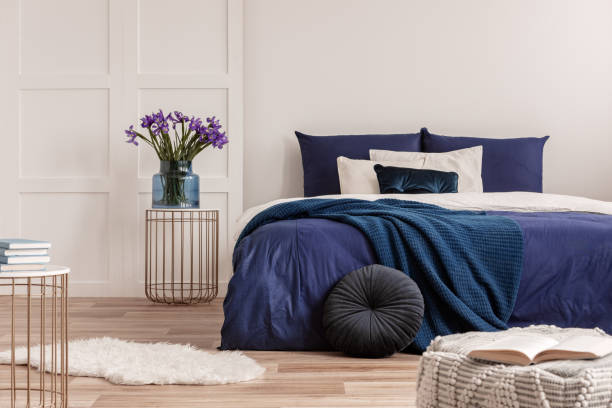 istock Flowers in vase on bedside table next to king size bed with navy blue bedding 1162202553