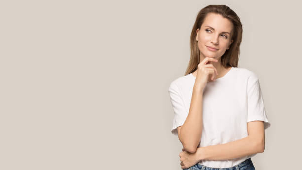Thoughtful young woman touching chin, looking aside at copy space