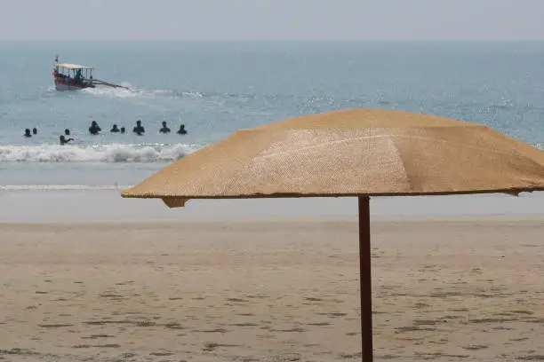Stock photo showing parasols on Palolem Beach, Goa, India with holidaymakers swimming in the sea viewable in the distance.