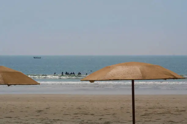 Stock photo showing parasols on Palolem Beach, Goa, India with holidaymakers swimming in the sea viewable in the distance.