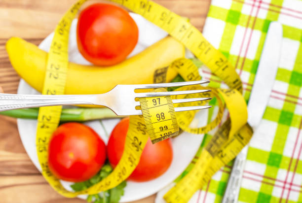 istock Fork with measuring tape over table with fresh fruit and vegetables. Healthy eating and dieting. 1162204075
