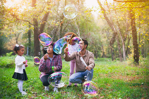 Happy family playing soap bubbles in park.