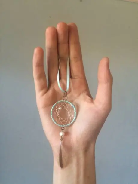 human hand delicately holding a hand made crafted dream catcher
