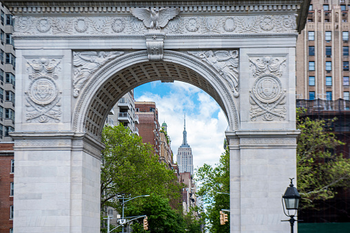 Partial view of the Washington Square marble arch during a summer day in Greenwich Village, Manhattan, New York City, USA. At the background, the Empire State building.