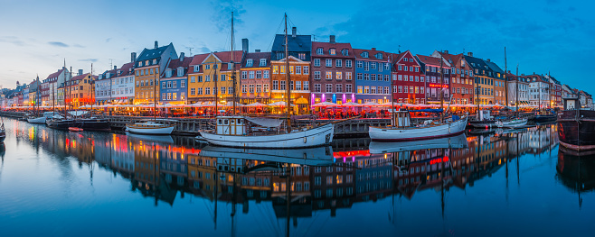 Cool blue dusk sky above the warm lights of Nyhavn, the iconic harbour restaurants and bars in the heart of Copenhagen, Denmark’s vibrant capital city.