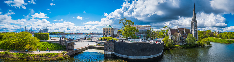 Tourists enjoying the spring sunshine  in Copenhagen’s historic harbour beneath the spire of St. Alban's Church, Denmark.