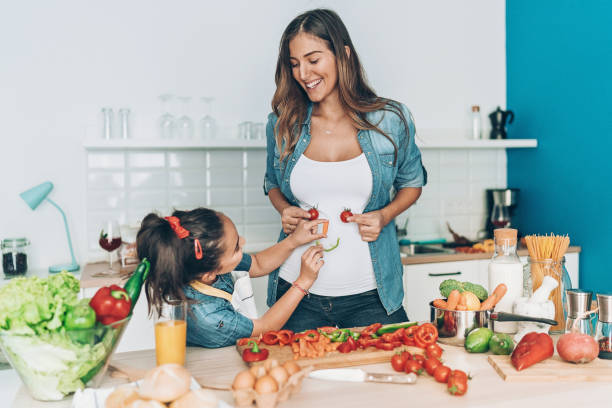 Pregnant mother and daughter making vegetable smiley face Pregnant Mother and her daughter playing in the kitchen abdomen stock pictures, royalty-free photos & images