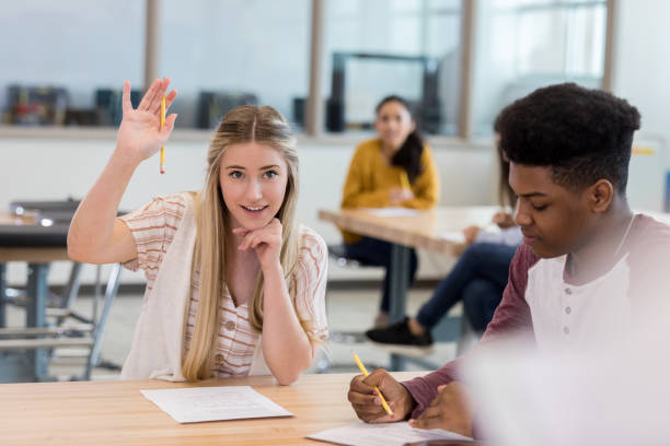 Teenage girl asks question during class Cute teenage girl raises hand to ask or answer a question during class. teenage high school girl raising hand during class stock pictures, royalty-free photos & images