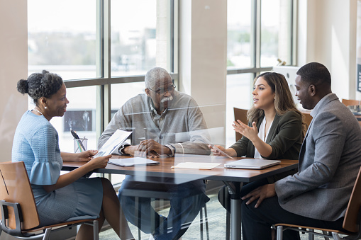 Mid adult Hispanic woman gestures as she discusses something with a lawyer. The woman is sitting next to her husband and father-in-law.