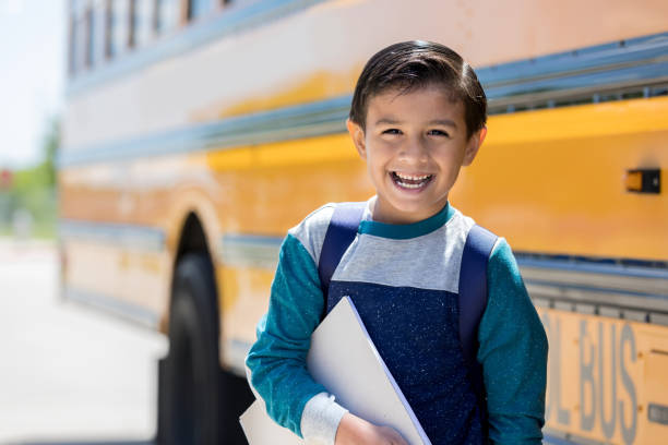 istock Elementary schoolboy smiles in front of school bus 1162215653