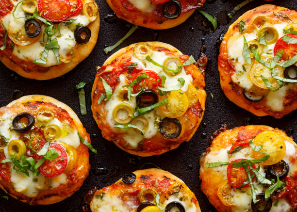 mini pizzas avec l'ajout de tomates cerises, olives, fromage mozzarella et basilic frais sur fond noir - tomato small food vegetable photos et images de collection