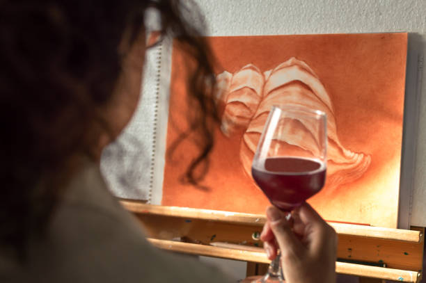 mulher que bebe um vidro do vinho para comemorar que terminou sua pintura. artista contemplando seu trabalho terminado. - artist young adult artists canvas adult - fotografias e filmes do acervo