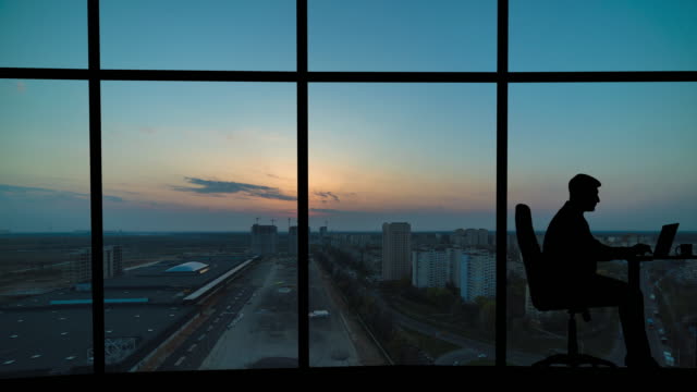 The man working near a panoramic window on a city background. time lapse