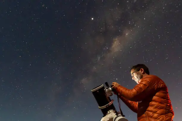 Photo of One astronomer man looking the night sky through an amateur telescope and taking photos with the Milky Way rising over the horizon, an amazing night view at Atacama Desert