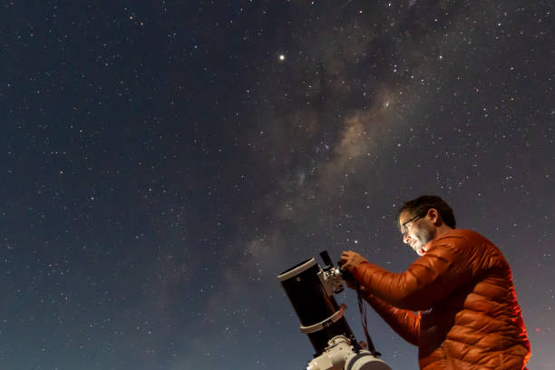 one astronomer man looking the night sky through an amateur telescope and taking photos with the milky way rising over the horizon, an amazing night view at atacama desert - astronomia imagens e fotografias de stock