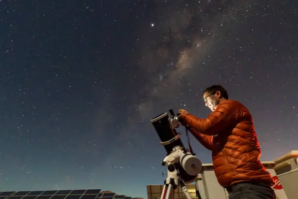 Photo of One astronomer man looking the night sky through an amateur telescope and taking photos with the Milky Way rising over the horizon, an amazing night view at Atacama Desert
