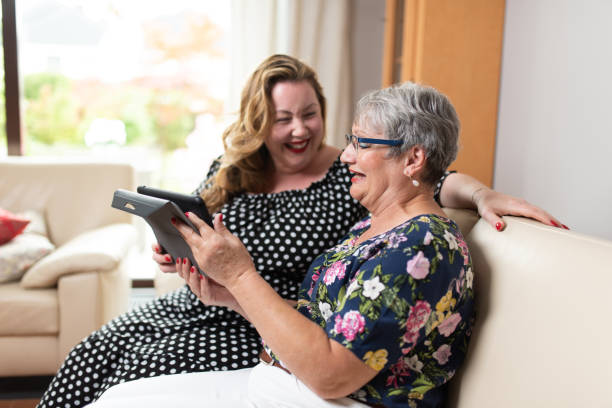 social media photoshoot Two women sitting on sofa watching social media and funny viral videos on a tablet. The overweight woman is laughing and the  elderly woman with short gray hair is holding a tablet pale complexion stock pictures, royalty-free photos & images