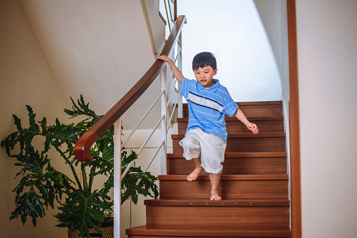 Young barefoot Taiwanese boy in casual clothing descending the staircase in a contemporary home interior.