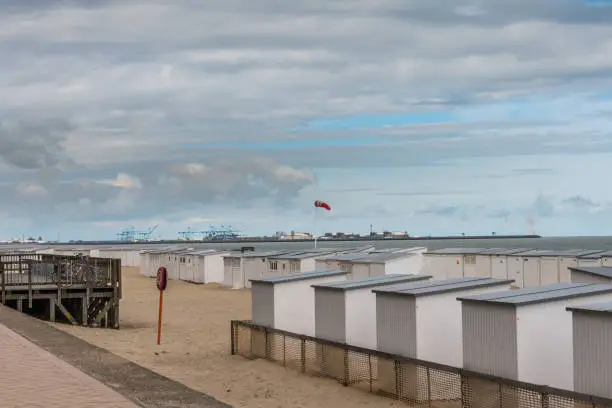 Knokke-Heist, Flanders, Belgium -  June 16, 2019: Knokke-Zoute part of town. Rows of white beach cabins on the sand with Zeebrugge LNG-sea terminal in back under pastel cloudscape.
