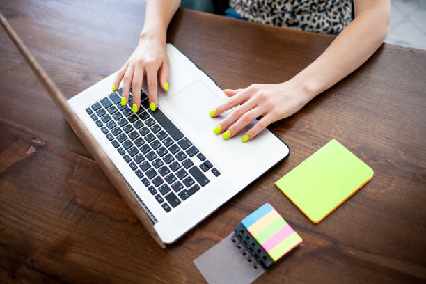 istock Women's hands with trend yellow manicure typing text on a laptop keyboard. 1162241629