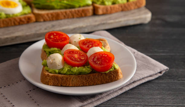 istock Tomato and Mozzarella Avocado Toast on a Dark Wood Table 1162245379