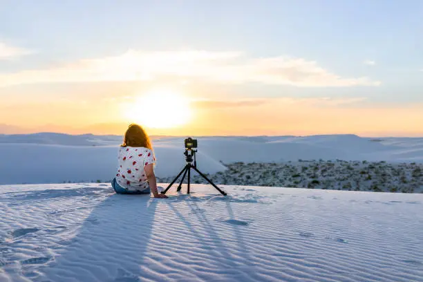 Woman girl photographer with tripod doing time lapse with camera in white sands dunes national monument in New Mexico view of sunset