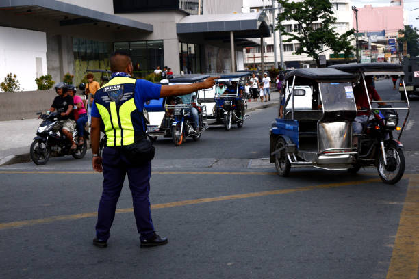 A traffic enforcer directs traffic to vehicles at a busy intersection ANTIPOLO CITY, PHILIPPINES – JULY 12, 2019: A traffic enforcer directs traffic to vehicles at a busy intersection in the business district of Antipolo City. philippines tricycle stock pictures, royalty-free photos & images