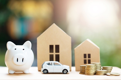 Piggy bank, Little toy car, money coins stacked on each other in different positions, house in paper model on the wooden table. Credit financial growing Loan to buy real asset concept. Saving money