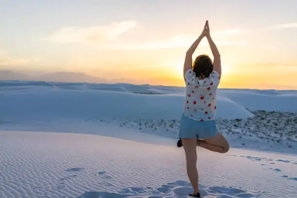 Girl woman back exercising balancing on one leg in white sands dunes national monument in New Mexico view of sunset