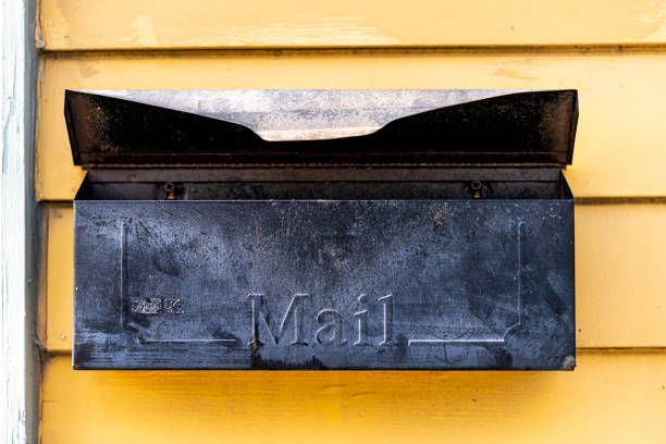 古いレトロなヴィンテージドアのメールボックス、ニューオーリンズ、ルイジアナ州で黄色で塗装された家の壁の外装に取り付けられたメールボックス - rusty yellow metal retro revival ストックフォトと画像