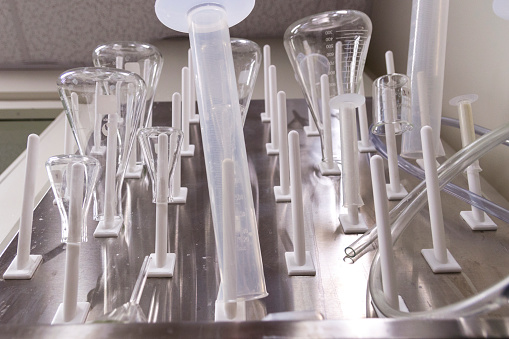 These are supplies for a chemistry laboratory in a classroom at a university. Glass beakers and measurement tubes are drying on a stainless steel rack above a sink.