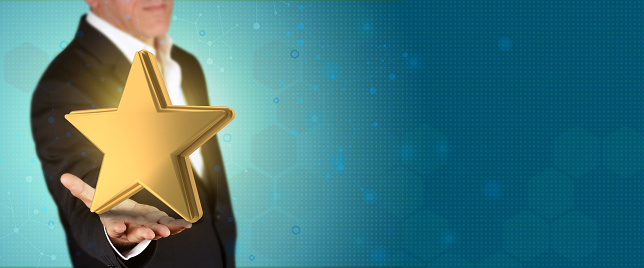 Businessman in suit, no tie, holds 3D gold star  object in his hand in front of blue technological background with large copy space. Business and Finance Concept.