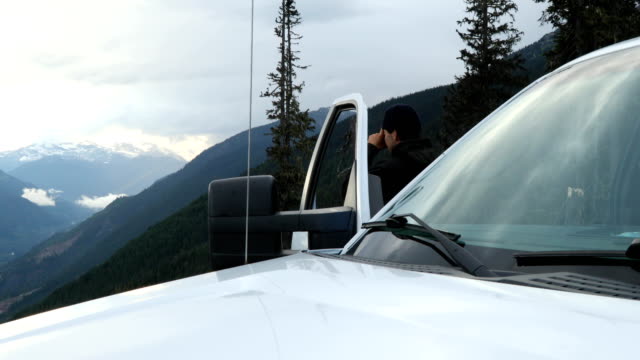 Young man pauses next to his vehicle to take photo of wild mountain scene