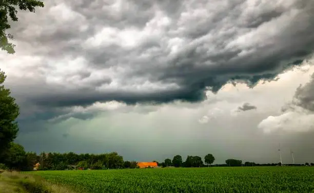 Farm and corn crop field looking small under immense threatening stormy clouds