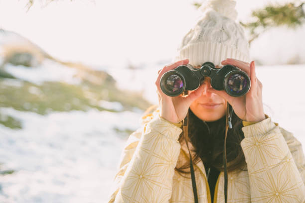 istock The girl in a White cap with a backpack in the winter in a forest looking through binoculars 1162270623