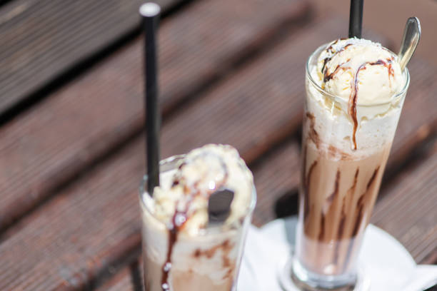 Ice coffee on a wood table with cream being poured into it showing the texture and refreshing look of the drink.