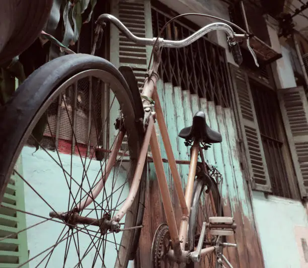 Amazing close up old bicycle front of antique house, wheel of bike rust, damaged with blurred background in vintage tone at China town, Vietnam